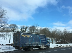 A blue Aspray lorry driving on the roads in the snow.