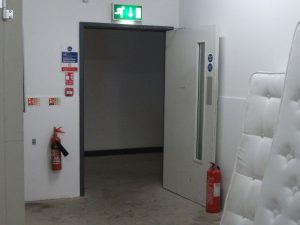 An open fire exit door with a fire extinguisher hung on the wall.