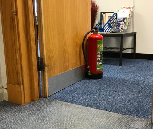 Image of a fire door being held open by a fire extinguisher
